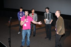 a man in a pink T Shirt Speaking with four other men