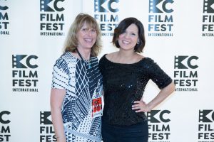 two women standing next to the KC Film Fest Poster