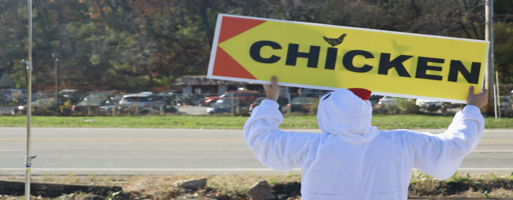 A person in white clothes holding a Chicken Banner